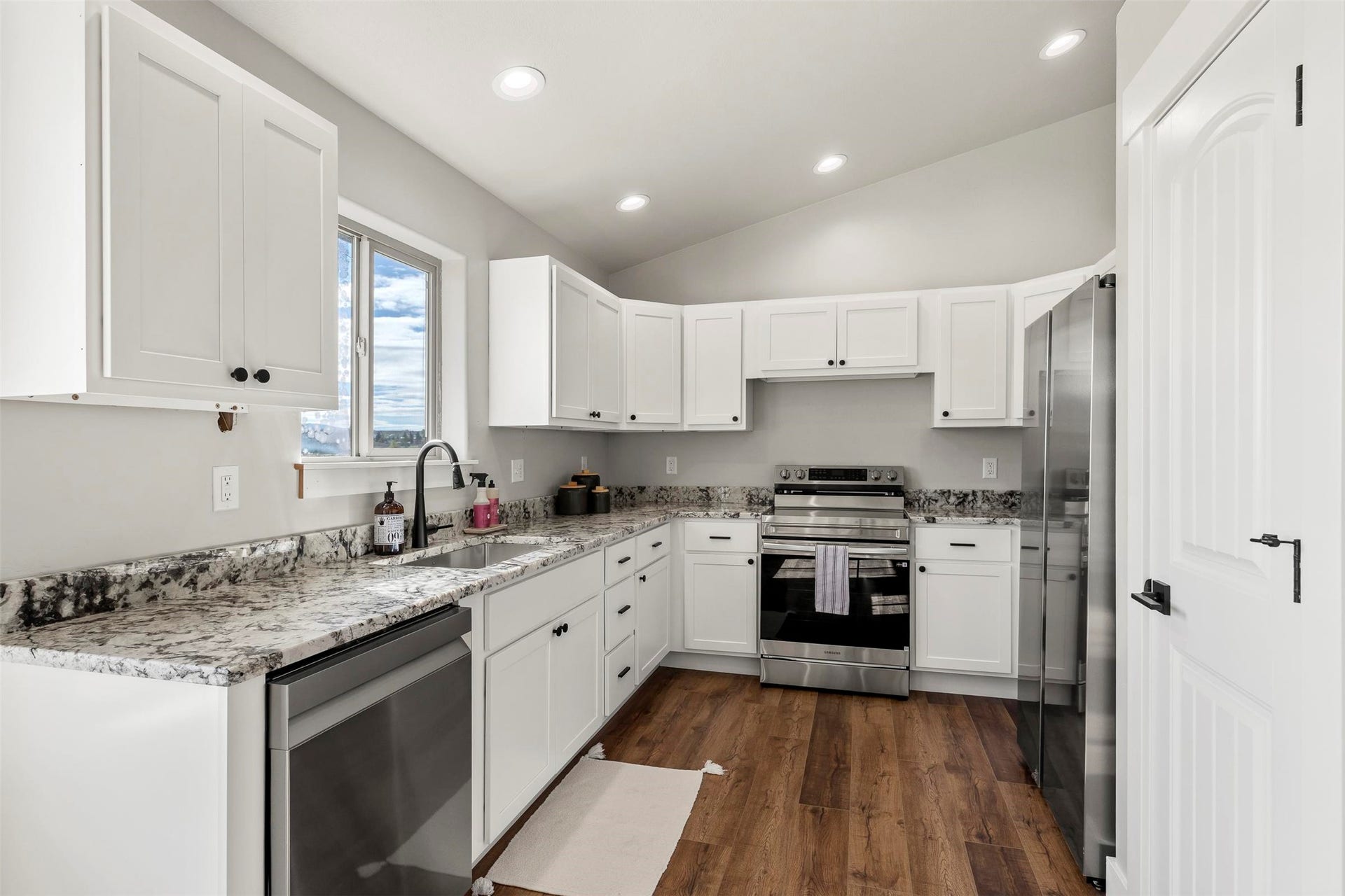 Kitchen featuring white cabinetry, stainless steel appliances, wood-finish flooring, recessed lighting, and a vaulted ceiling