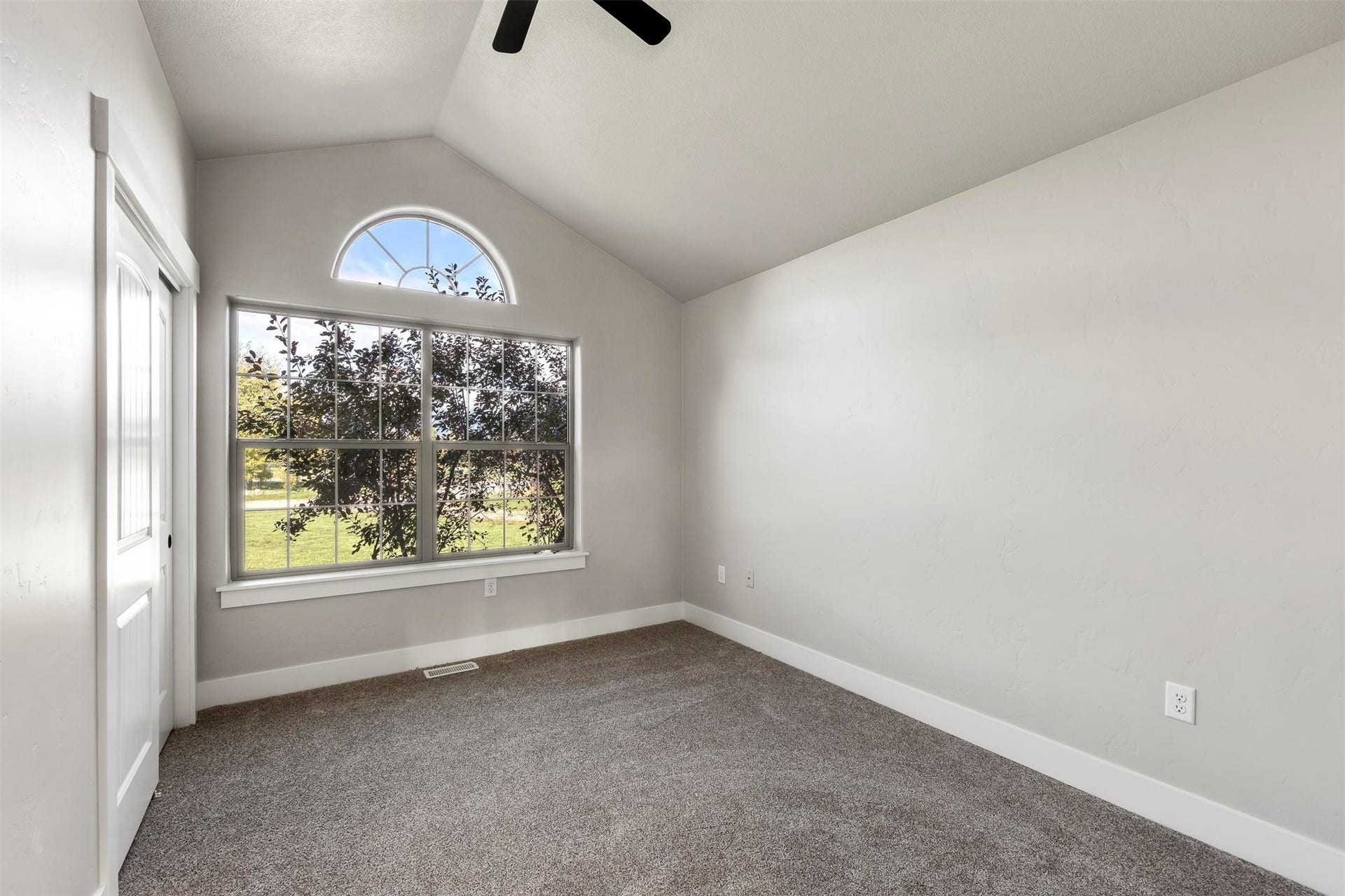 Vaulted ceiling with ceiling fan, large window with arched transom, and light gray wall paint