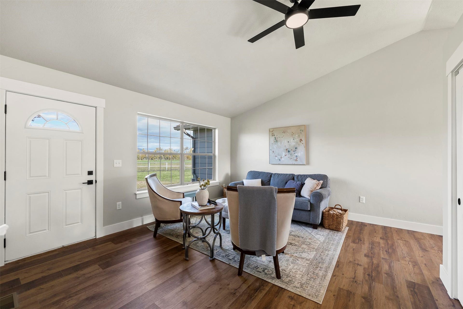Vaulted ceiling with a ceiling fan, wood-finish flooring, and a window with exterior landscape