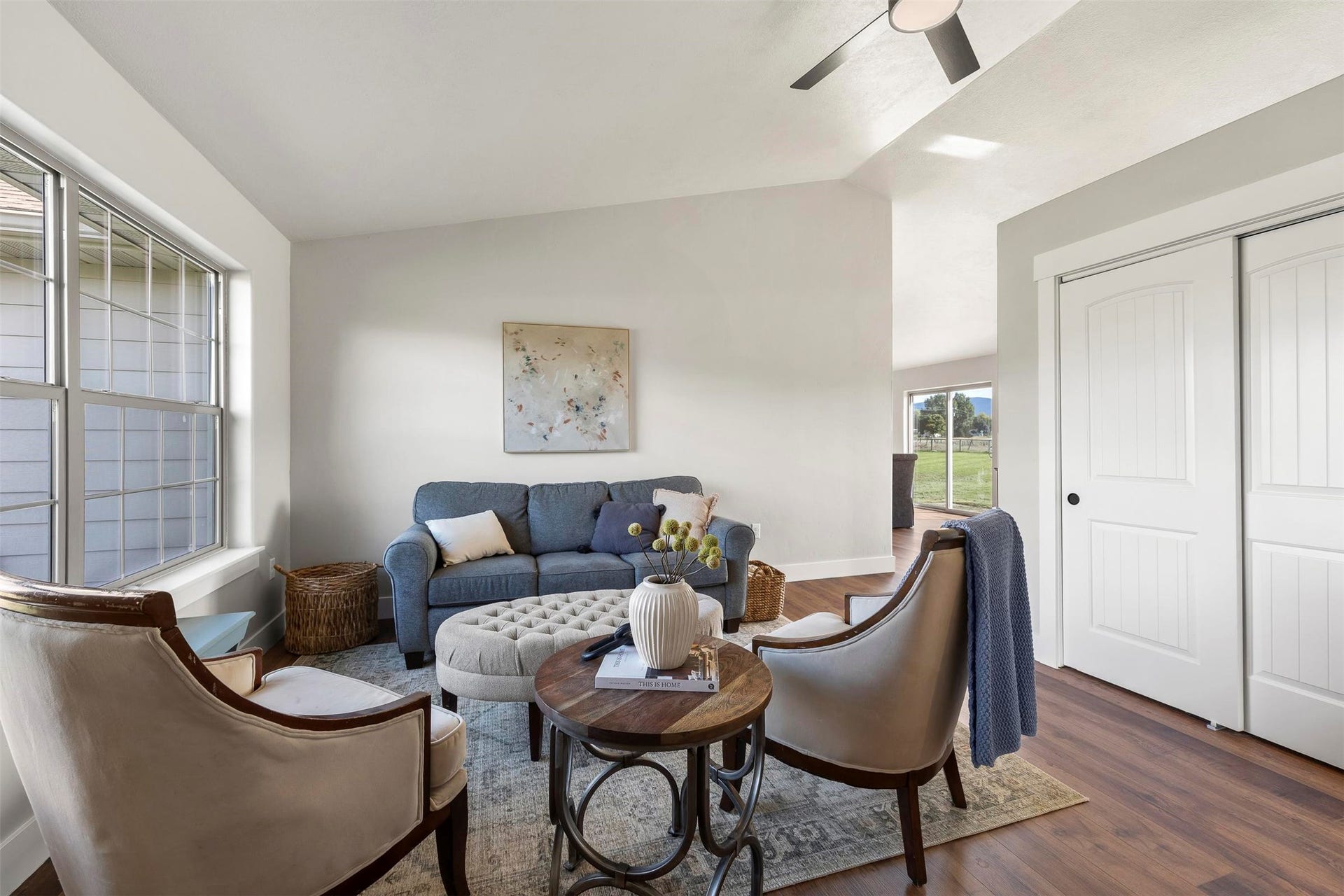 Vaulted ceiling with a flush-mount ceiling fan, wood-finish flooring, white sliding closet doors, and a large window with grilles