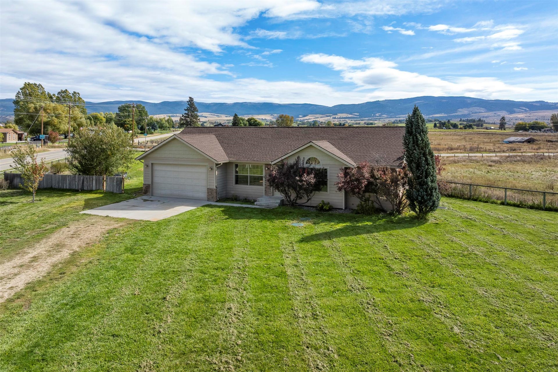 Exterior featuring a two-car garage, established front landscaping, a paved driveway, and a spacious green lawn