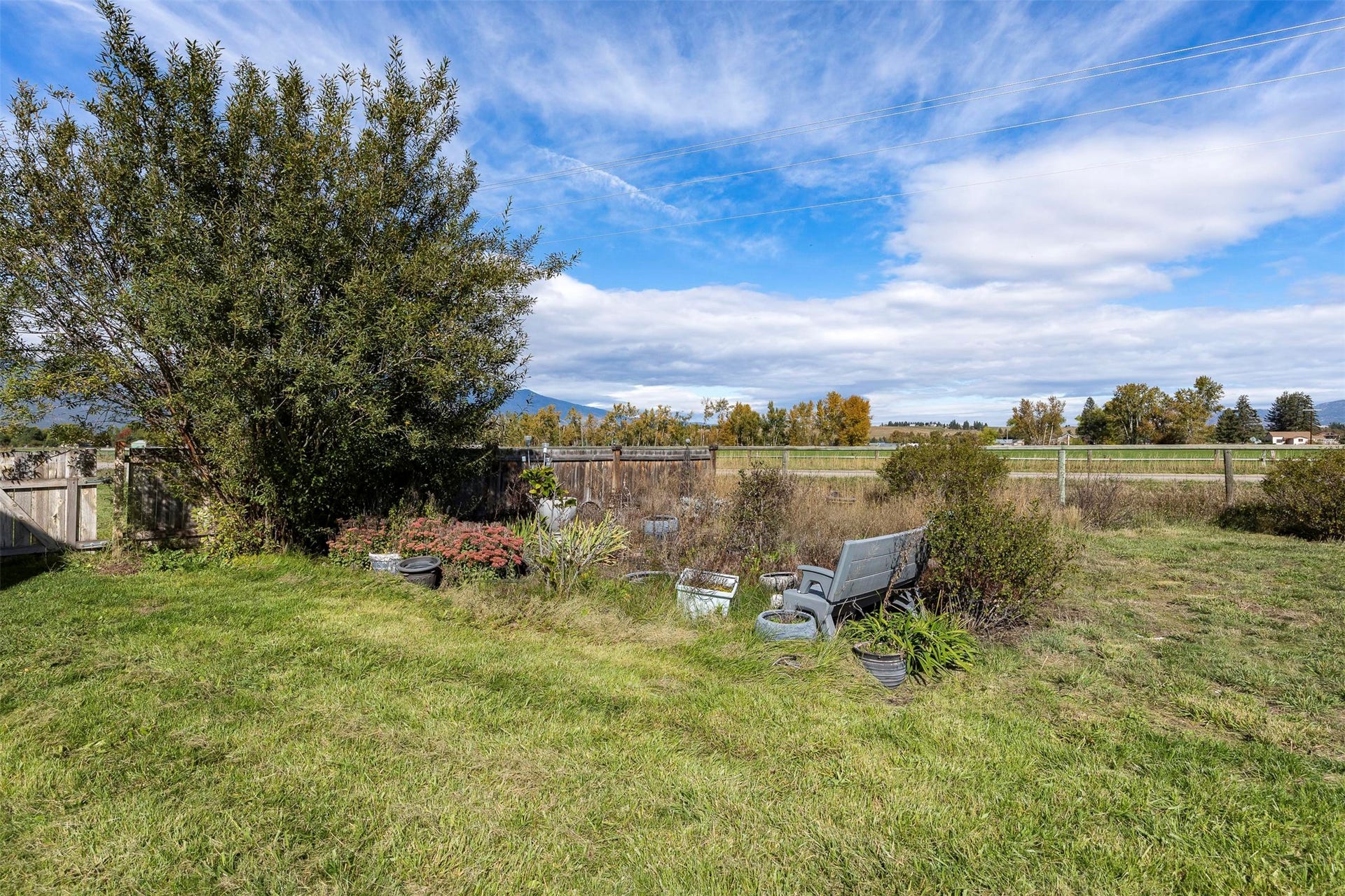 Expansive grassy area with mature foliage, a wood fence, and distant mountain scenery