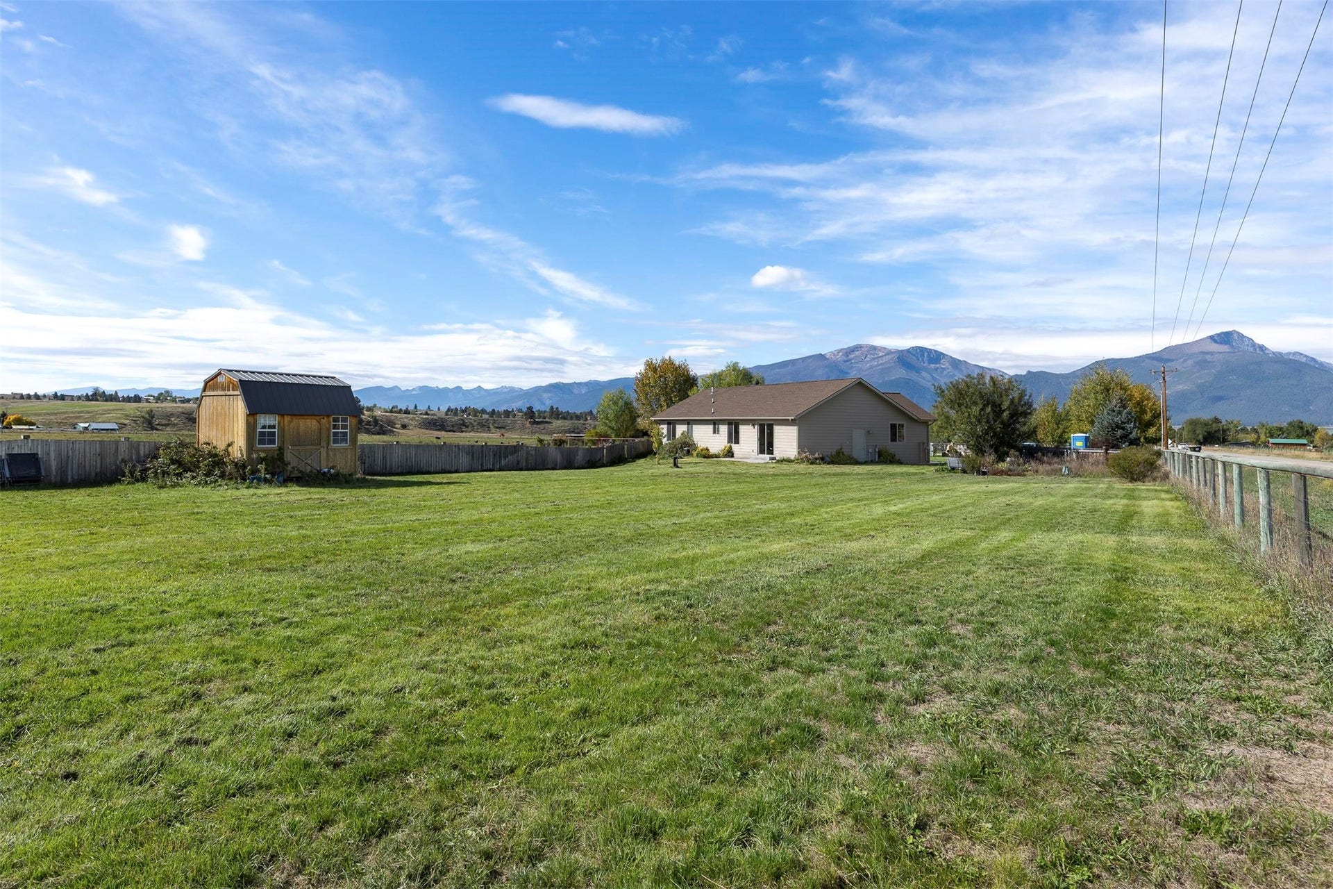 Expansive fenced yard with a detached storage shed, mature trees, and a mountain backdrop