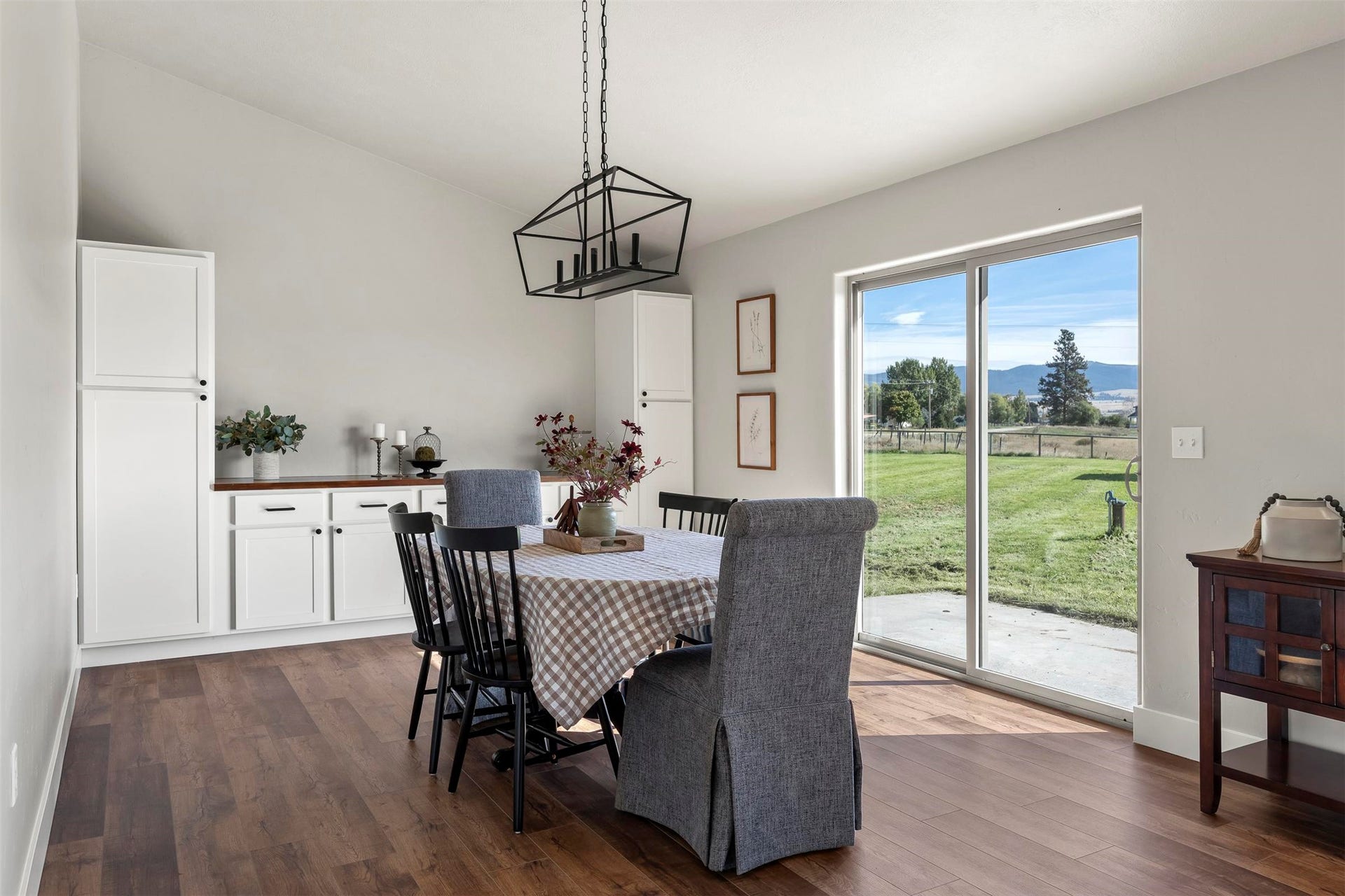 Vaulted ceiling, wood-finish flooring, white built-in cabinetry, sliding glass door, and a geometric chandelier