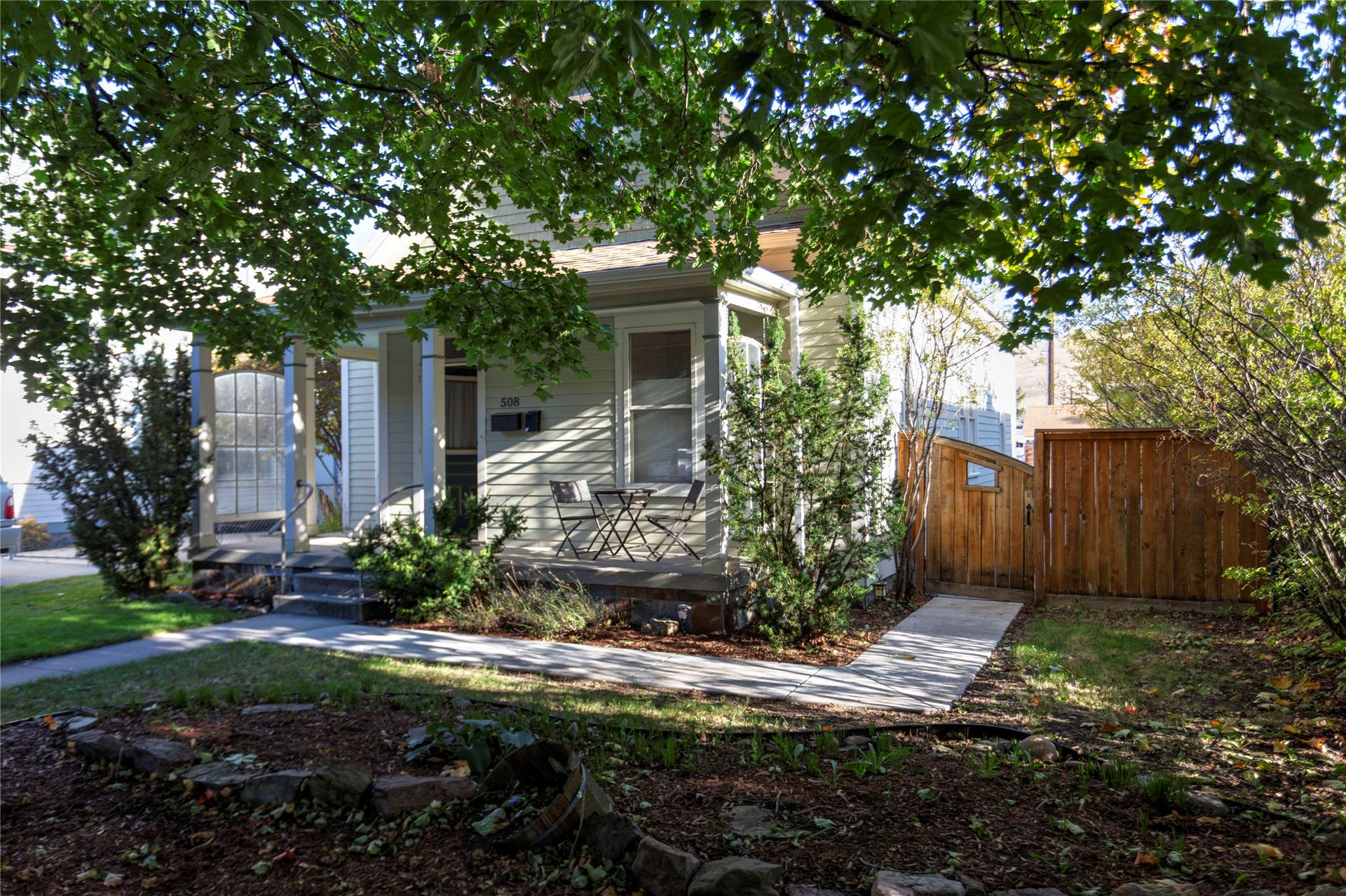 Siding exterior with a covered porch, mature trees, concrete walkway, and a wood fence