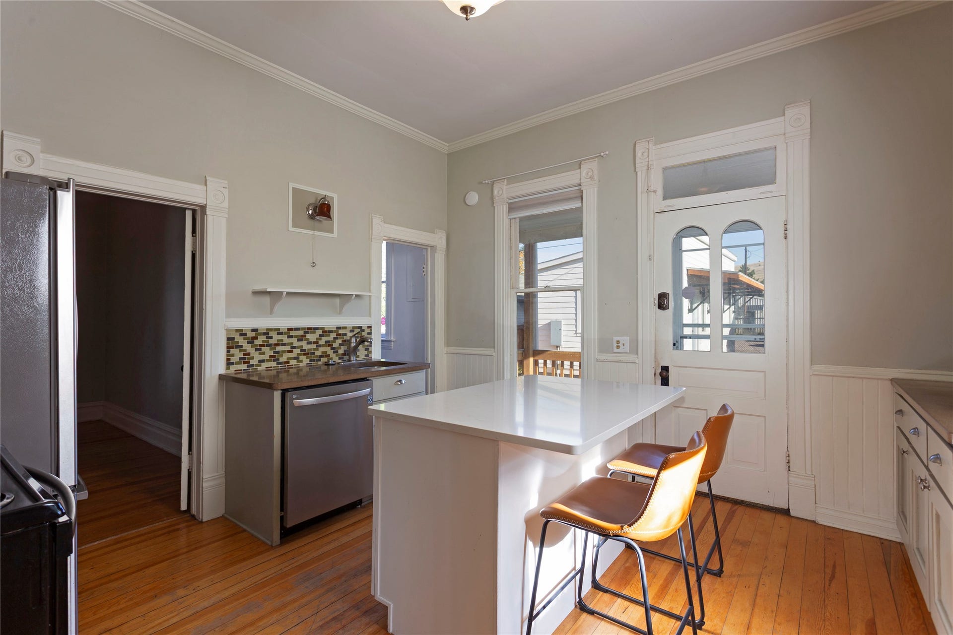 Wood-finish flooring, white island with a solid surface countertop, stainless steel dishwasher, decorative tile backsplash, and a multi-pane glass door