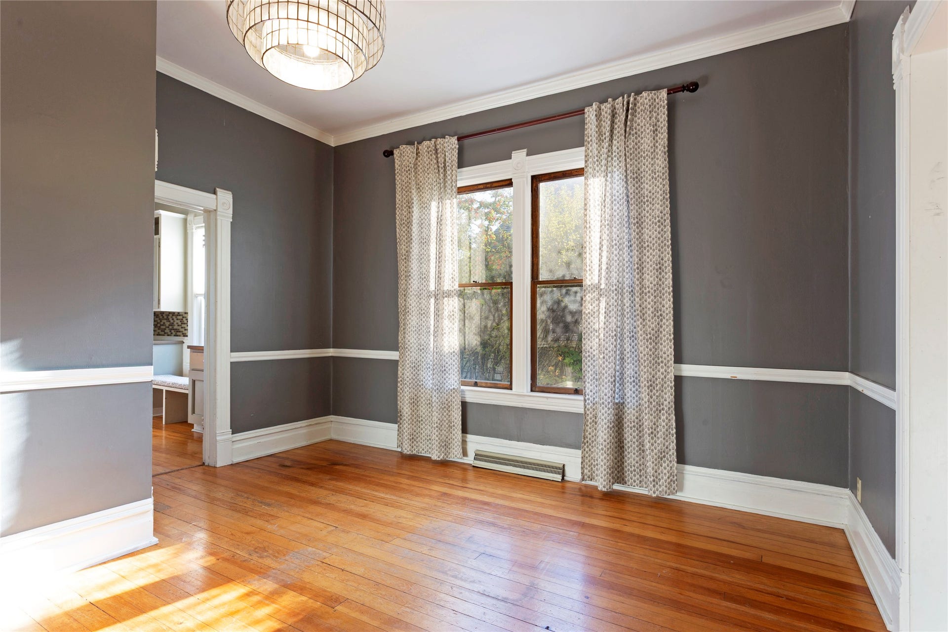 Hardwood flooring, crown molding, wall paneling, dual windows, and an overhead drum light fixture