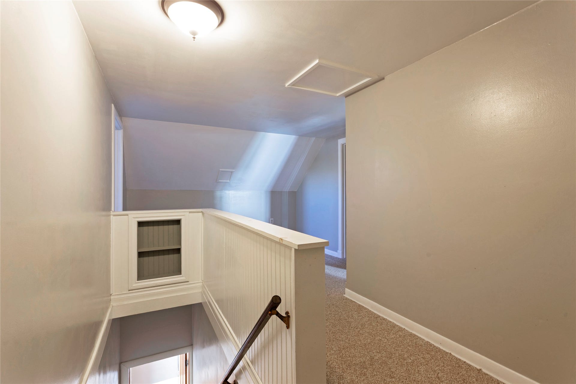 Carpeted hallway with painted walls, recessed lighting, and a wood handrail