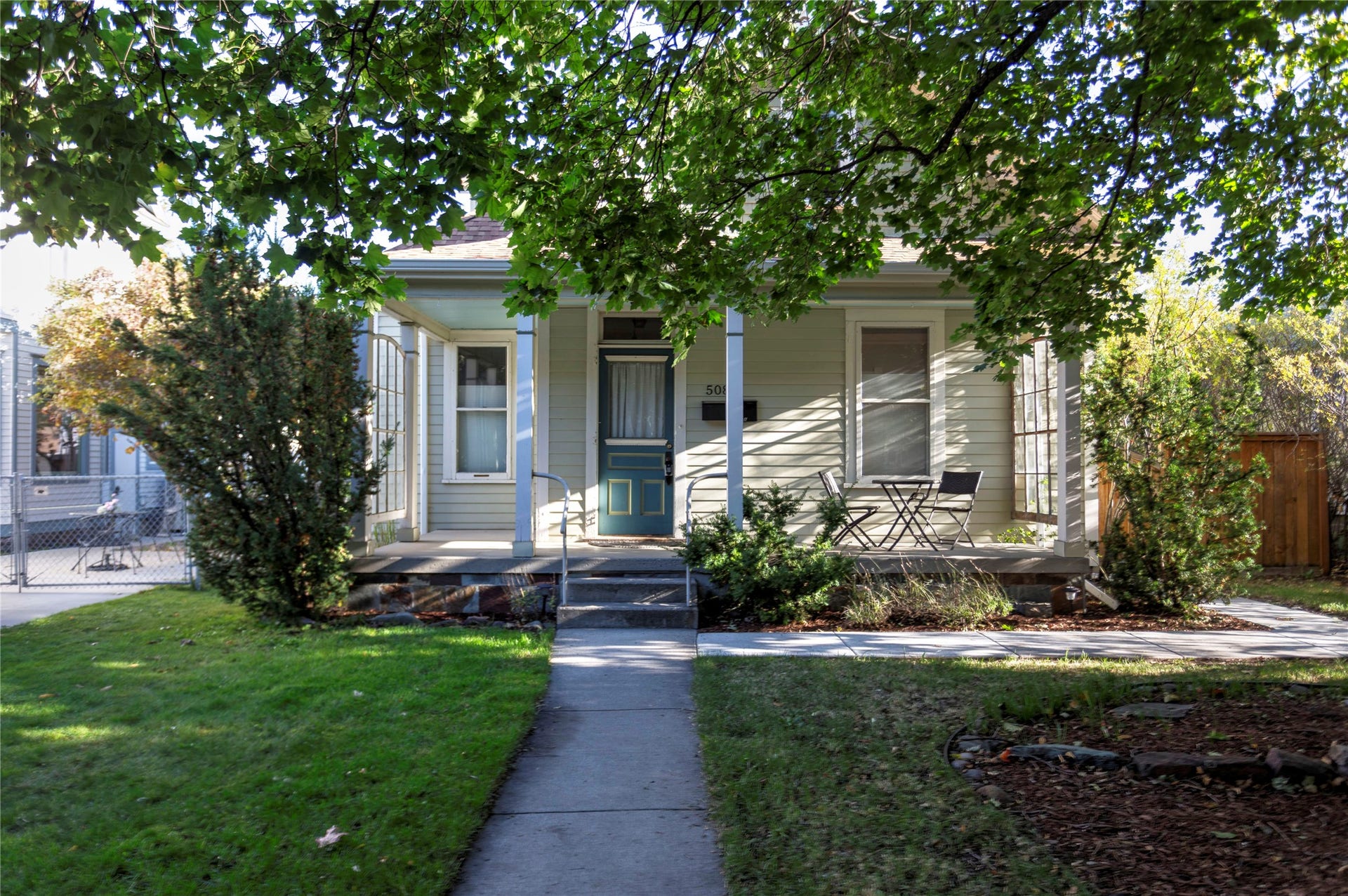 Light-colored horizontal siding, covered front porch, dark-colored entry door, concrete pathway, and established front landscaping