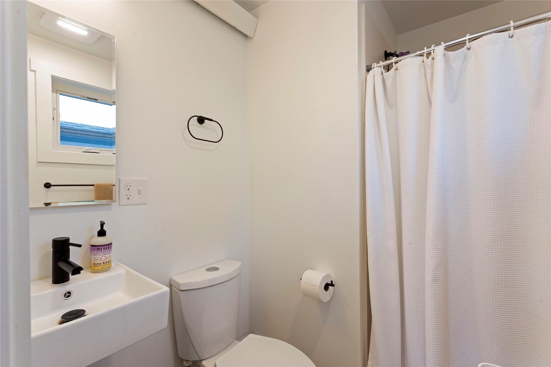 Compact bathroom featuring a white wall-mounted sink with a matte black faucet, a framed mirror, and a toilet