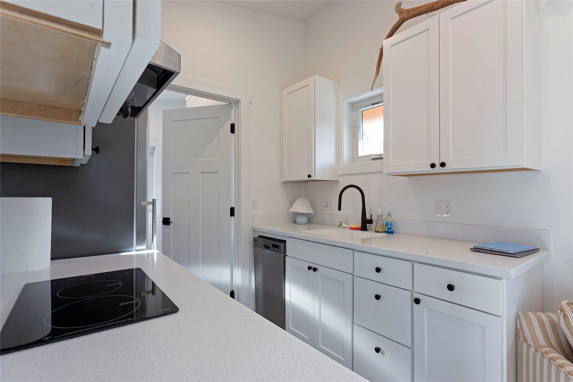 White cabinetry with black hardware, integrated cooktop, stainless steel dishwasher, and a black gooseneck faucet