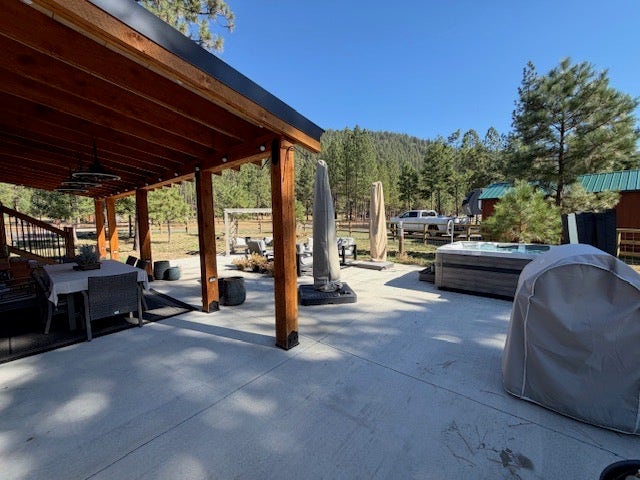 713 Shyrock Loop Dr., Superior, MT 59872 Expansive concrete patio featuring a wood-beamed covered porch, above ground hot tub, and surrounding mature trees