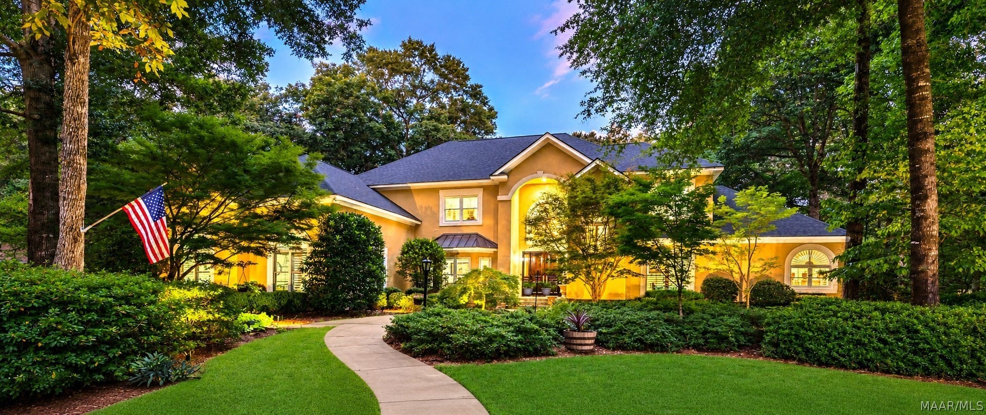 Striking twilight view showcases the homes impressive architecture, warm exterior lighting and beautifully landscaped, tree-lined setting.