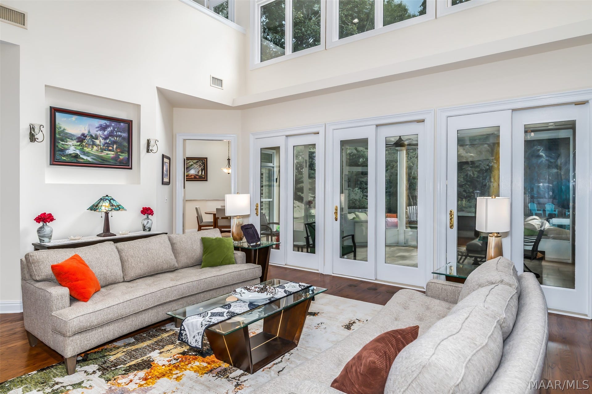 A dramatic, light-filled living space with soaring ceilings with a walls of windows overlooking the lush backyard and pool.