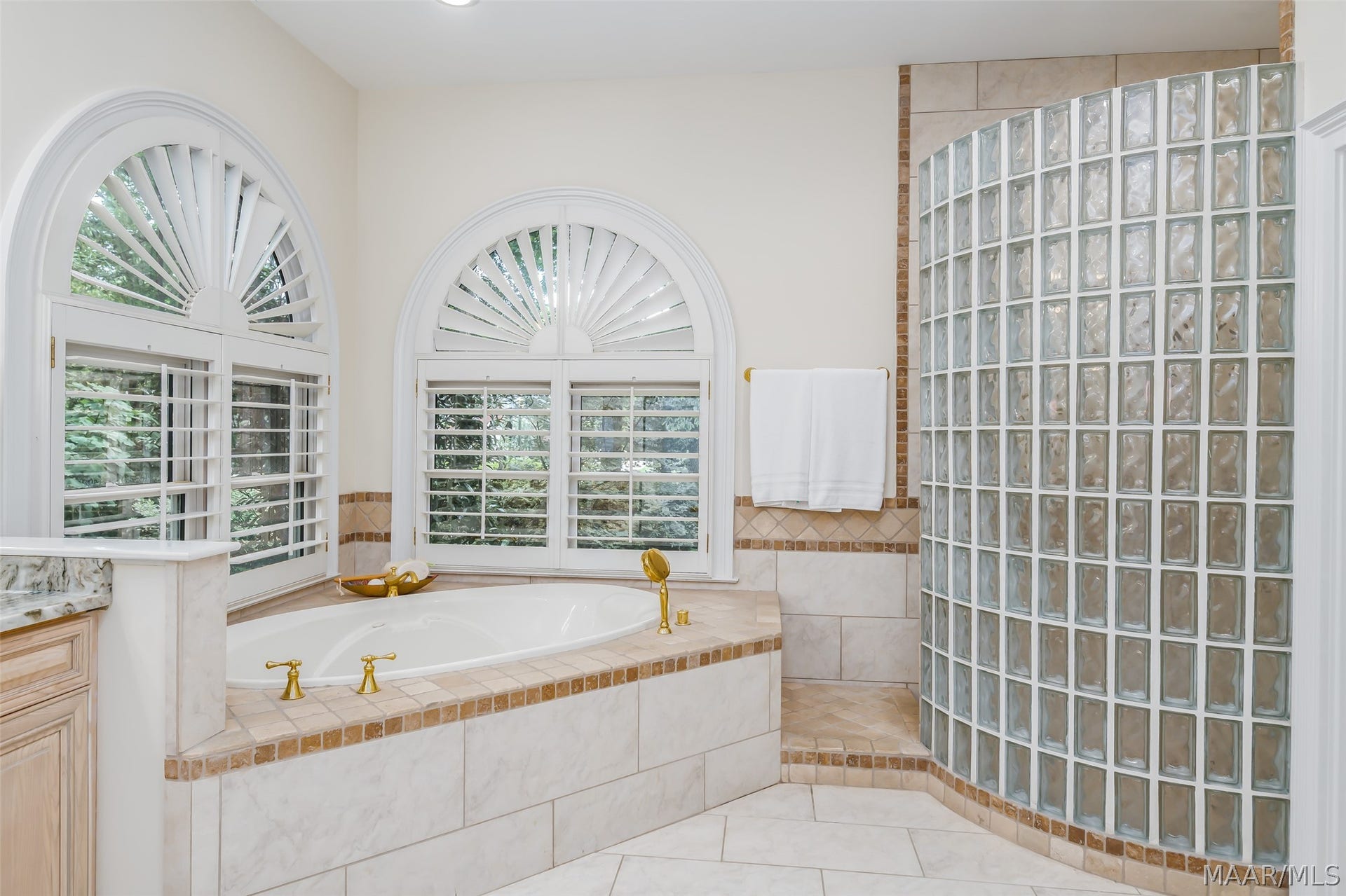 Spa-like owners bath featuring a soaking tub framed by distinctive arched windows and a spacious curved glass-block shower.