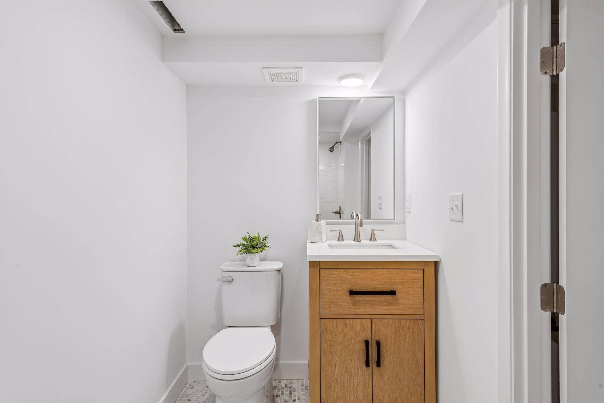 Lower Level 3/4 bathroom with updated Subway tile shower, White oak vanity with quartz top and Room and Board Mirror, New toilet, New lighting, and Marble flooring