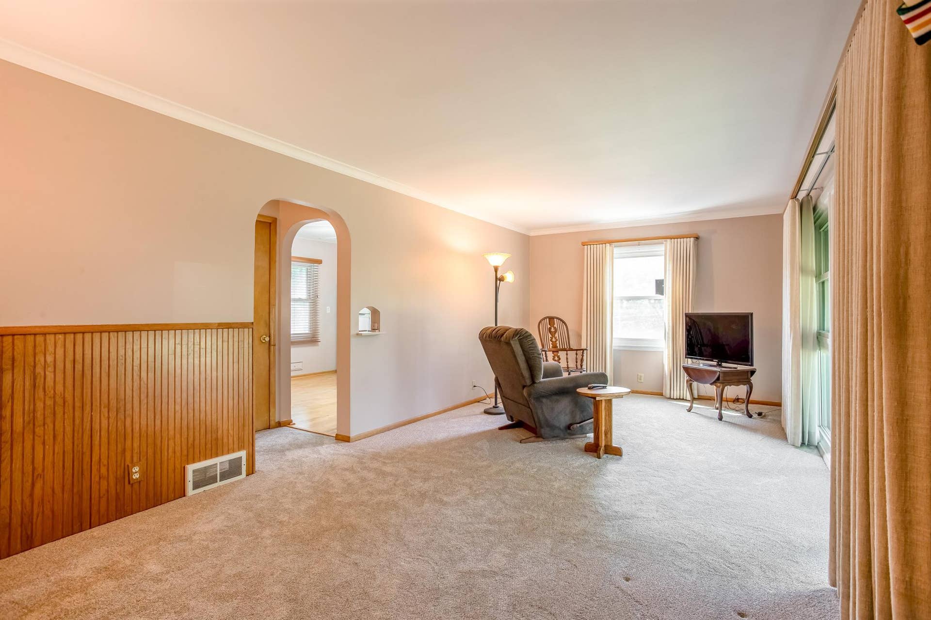 Another view of the generously sized living room highlights the open layout, crown molding, and charming arched doorway leading to the adjoining spaces.