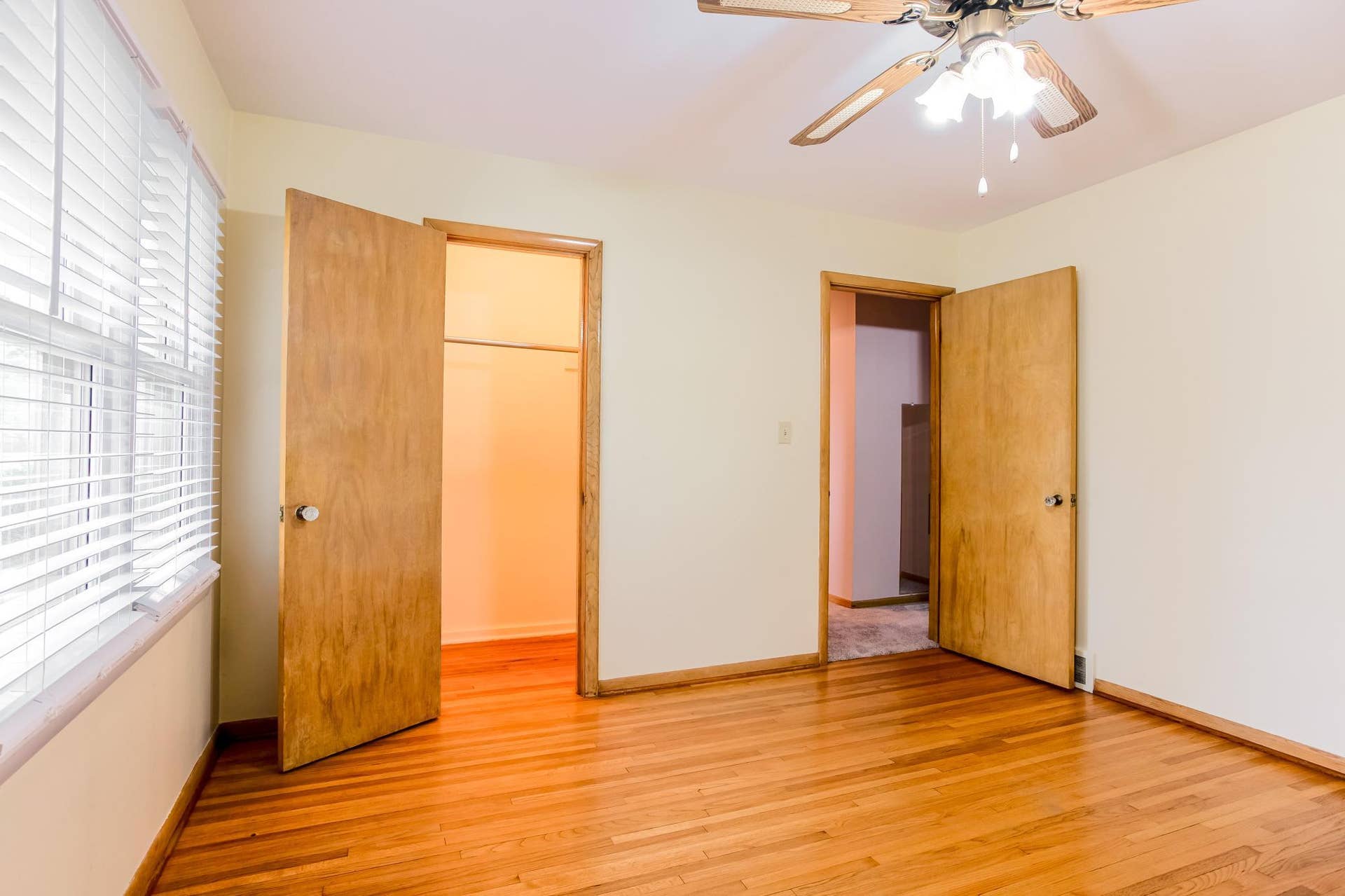 Spacious main-level bedroom with hardwood flooring, a ceiling fan, and large windows overlooking the back yard.