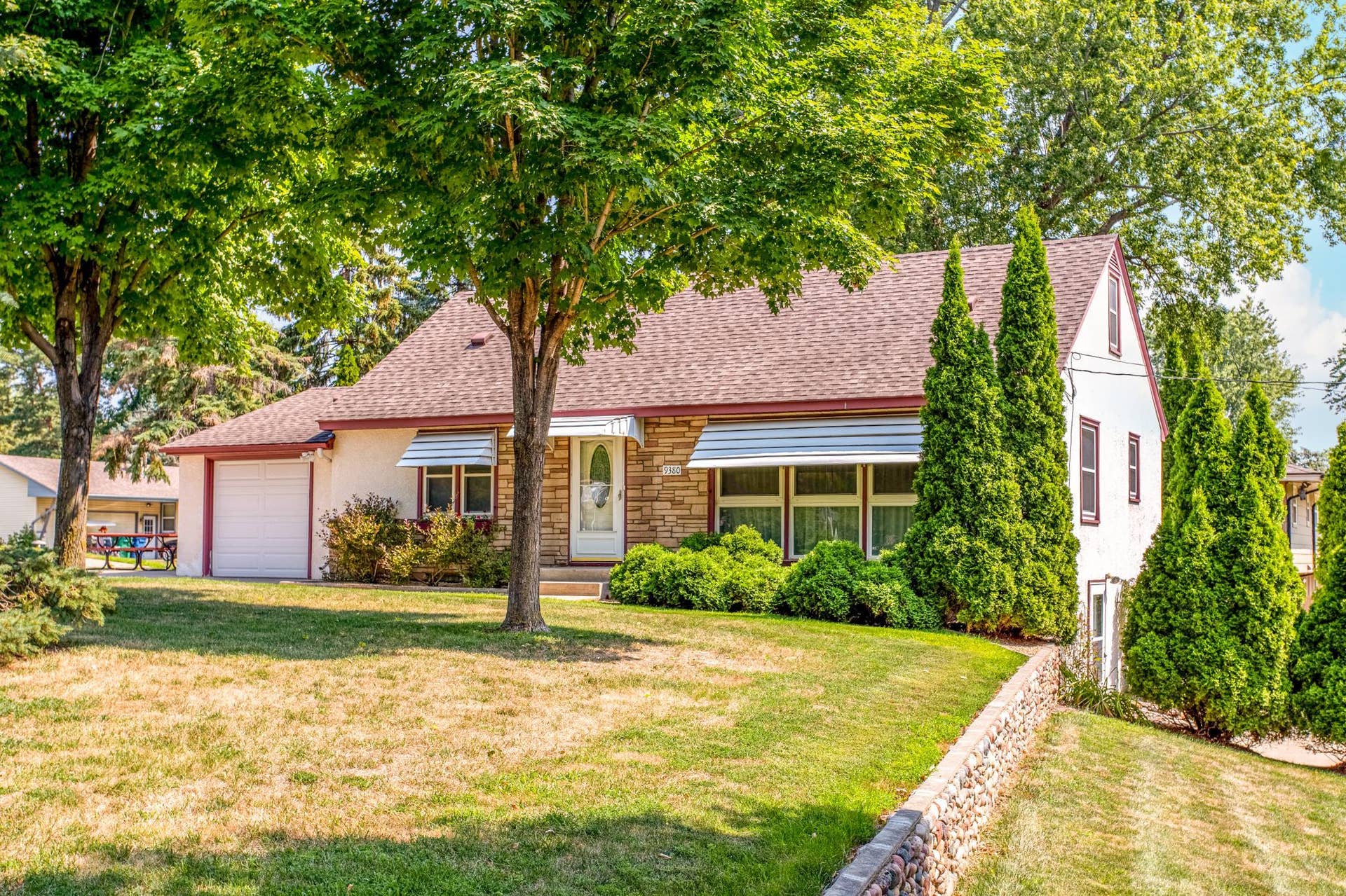 Beautiful curb appeal is enhanced by mature shade trees, established landscaping, and a welcoming exterior with classic stone accents.