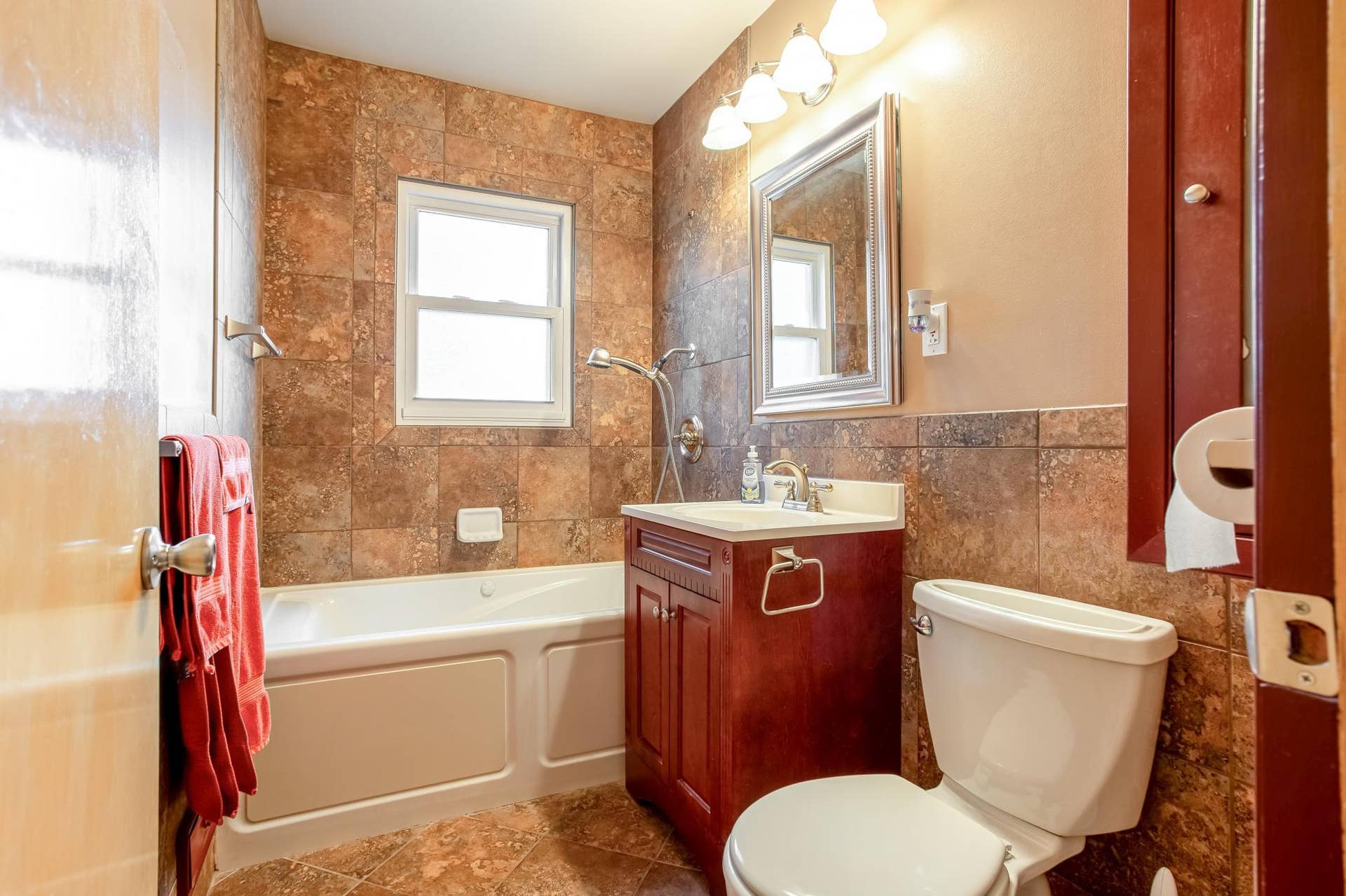 Updated full bathroom features extensive tilework, a jacuzzi tub/shower combination, and a window that brings in natural light.
