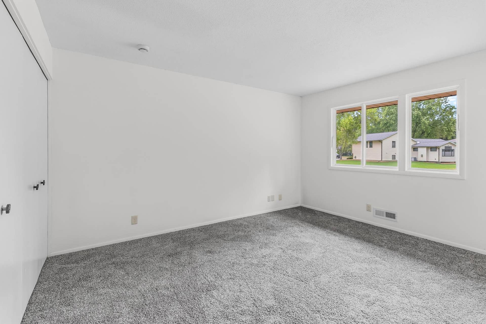 Spacious, light-filled bedroom featuring fresh neutral finishes, plush carpeting, generous closet space and a large window overlooking the neighborhood.