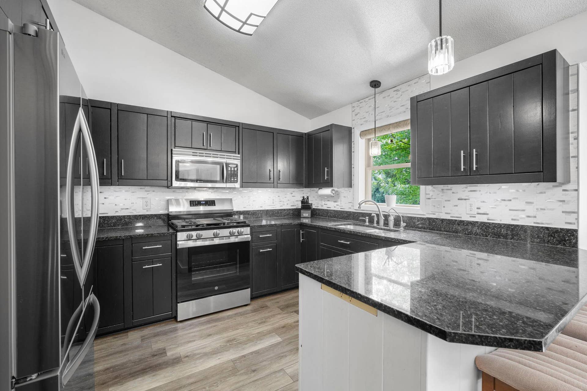 Wow! Gorgeous kitchen featuring classy black cabinetry, Granite countertops, Stainless Steel appliances, and a modern tiled backsplash.