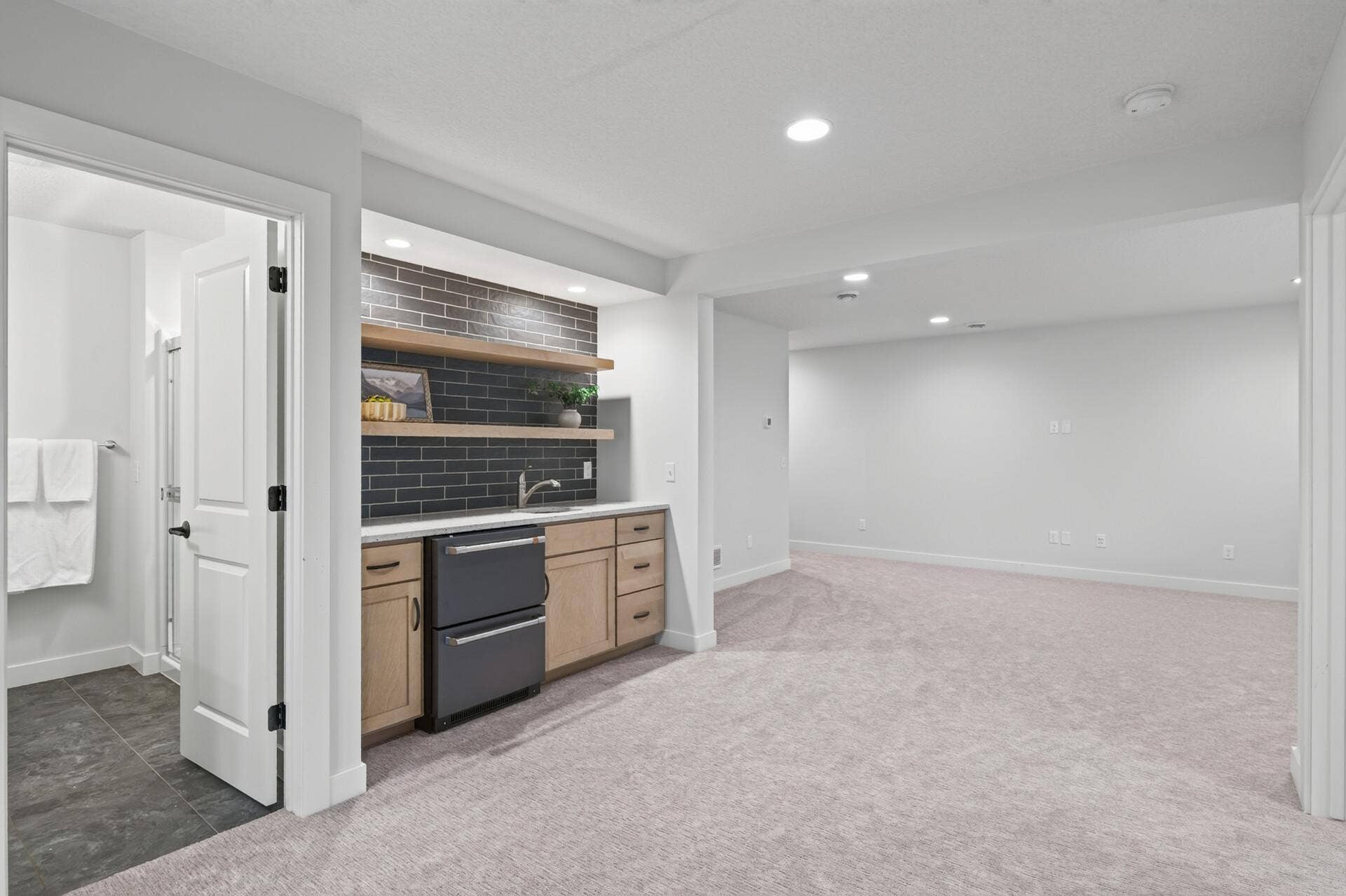 9960 Arrowwood Trail, Woodbury, MN 55129 A standout wet bar featuring beautifully designed dark tile, floating shelves, a sink, and a fridge; ideal for refreshments after sport court play.