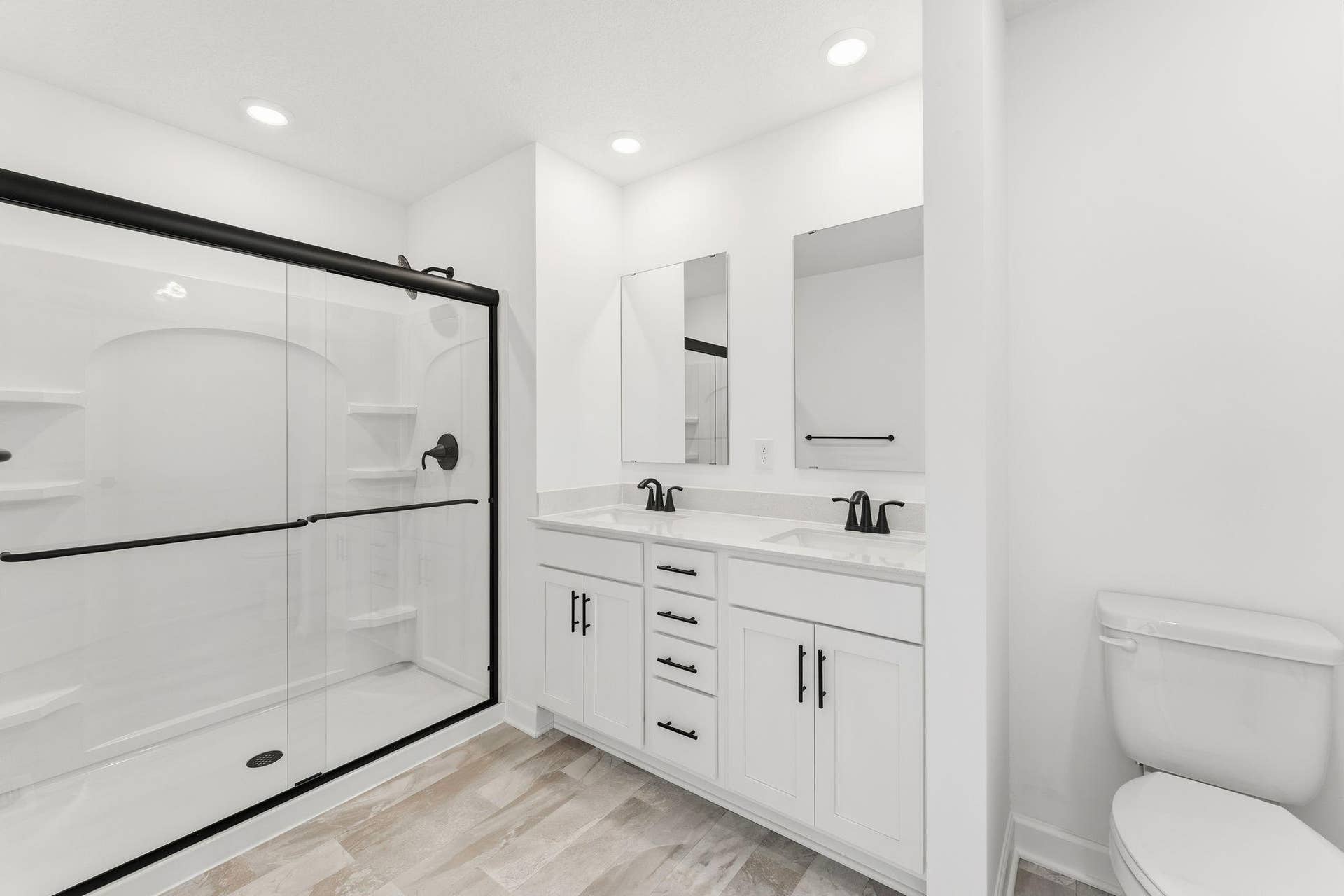 10551 Harbor Lane N, Maple Grove, MN 55369 (Photo of a similar home, actual finishes may vary) Featuring a glass-enclosed shower with built-in shelving and glass mirrors set atop dual quartz sinks and vanity-cabinetry, the en-suite bathroom helps streamline morning routines