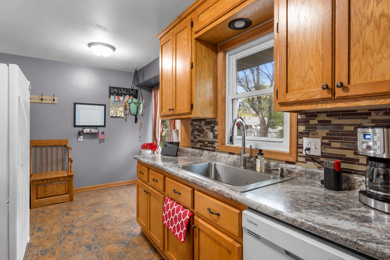 11833 Ilex Street NW, Coon Rapids, MN 55448 Warm wood cabinetry, a tile backsplash, and generous counter space complement a window above the sink overlooking the backyard