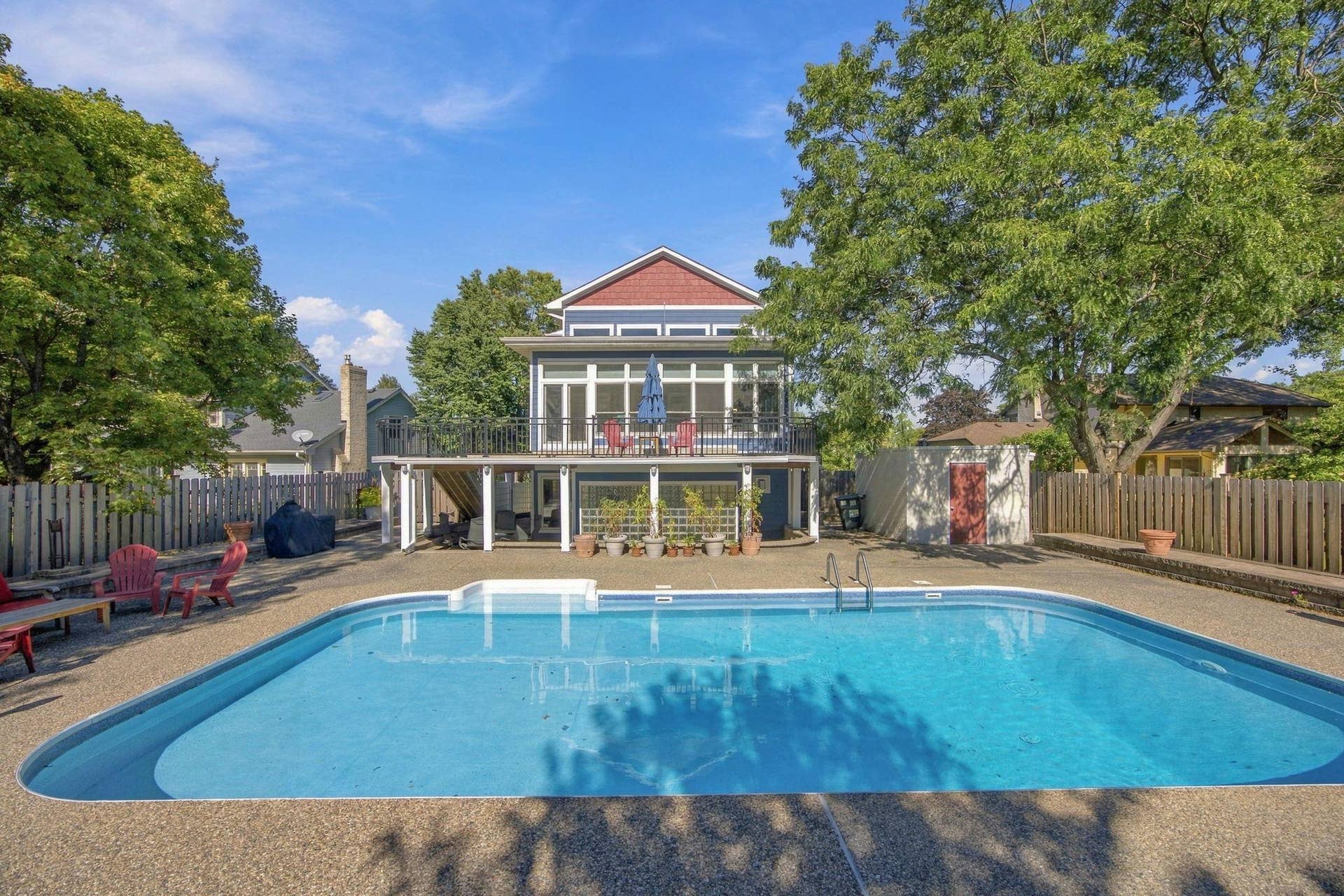 "Rear exterior showcasing the in-ground pool, wraparound deck, and heated four-season porch overlooking the backyard."