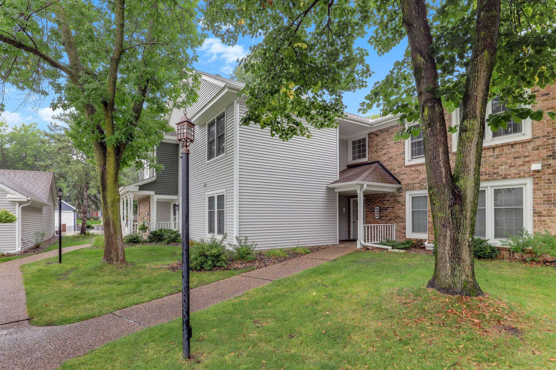 10966 Quebec Avenue S, Bloomington, MN 55438 Exterior view of 10966 Quebec Ave S featuring brick and vinyl siding, mature shade trees, lush green lawn, landscaped gardens, and winding sidewalks in a peaceful setting.