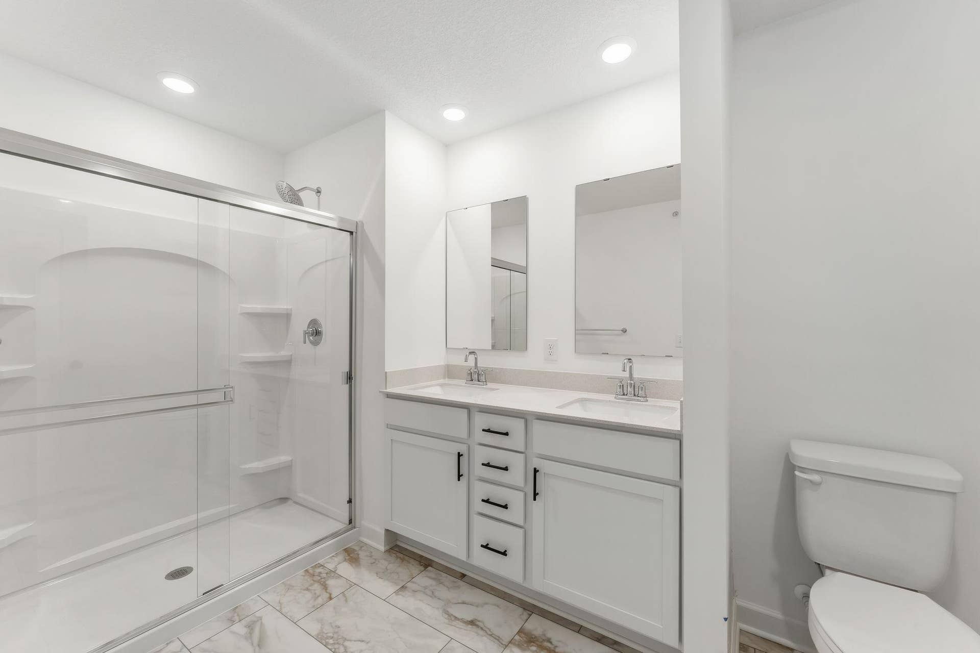 Featuring a glass-enclosed shower with built-in shelving and glass mirrors set atop dual quartz sinks and vanity-cabinetry, the en-suite bathroom helps streamline morning routines