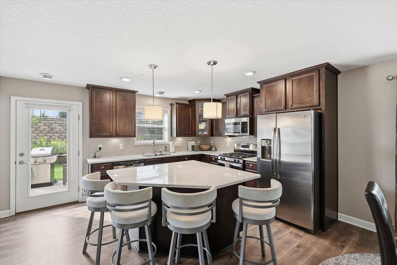 9757 5th Street Lane N, Lake Elmo, MN 55042 Quartz countertops, tiled backsplash, warm under-cabinet lighting, espresso cabinets, and over-sized island