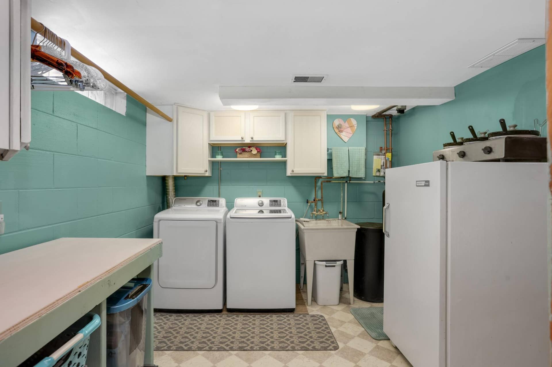 Neat and orderly laundry room offering utility sink, newer washer & dryer. Rolling table for folding/storage will stay with home.