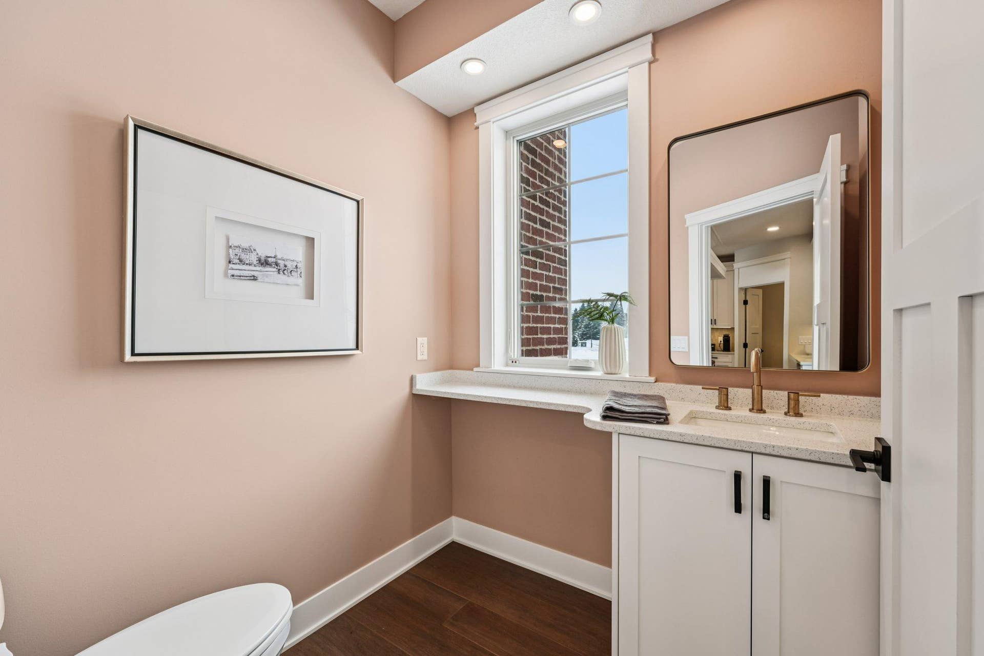Stylish main-level powder room with quartz vanity, modern fixtures, framed mirror, and warm accent wall color.