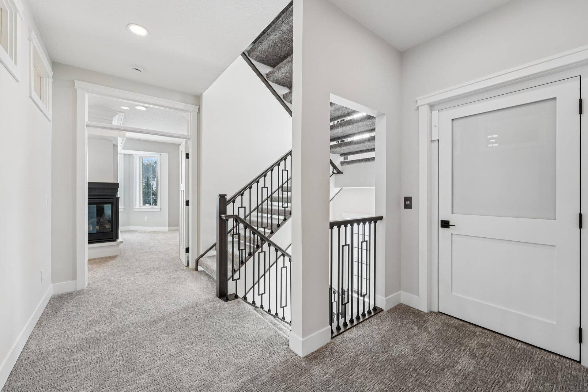 Open and bright upper-level hallway featuring plush carpeting, modern black iron railings, and clean architectural detailing that connects the living spaces with style.