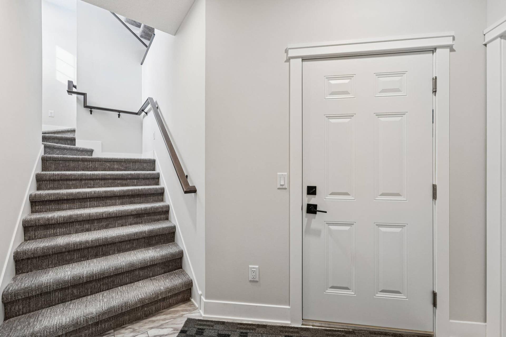 Lower-level stairway with plush carpeting and modern railing, providing easy access to the garage and additional spaces.