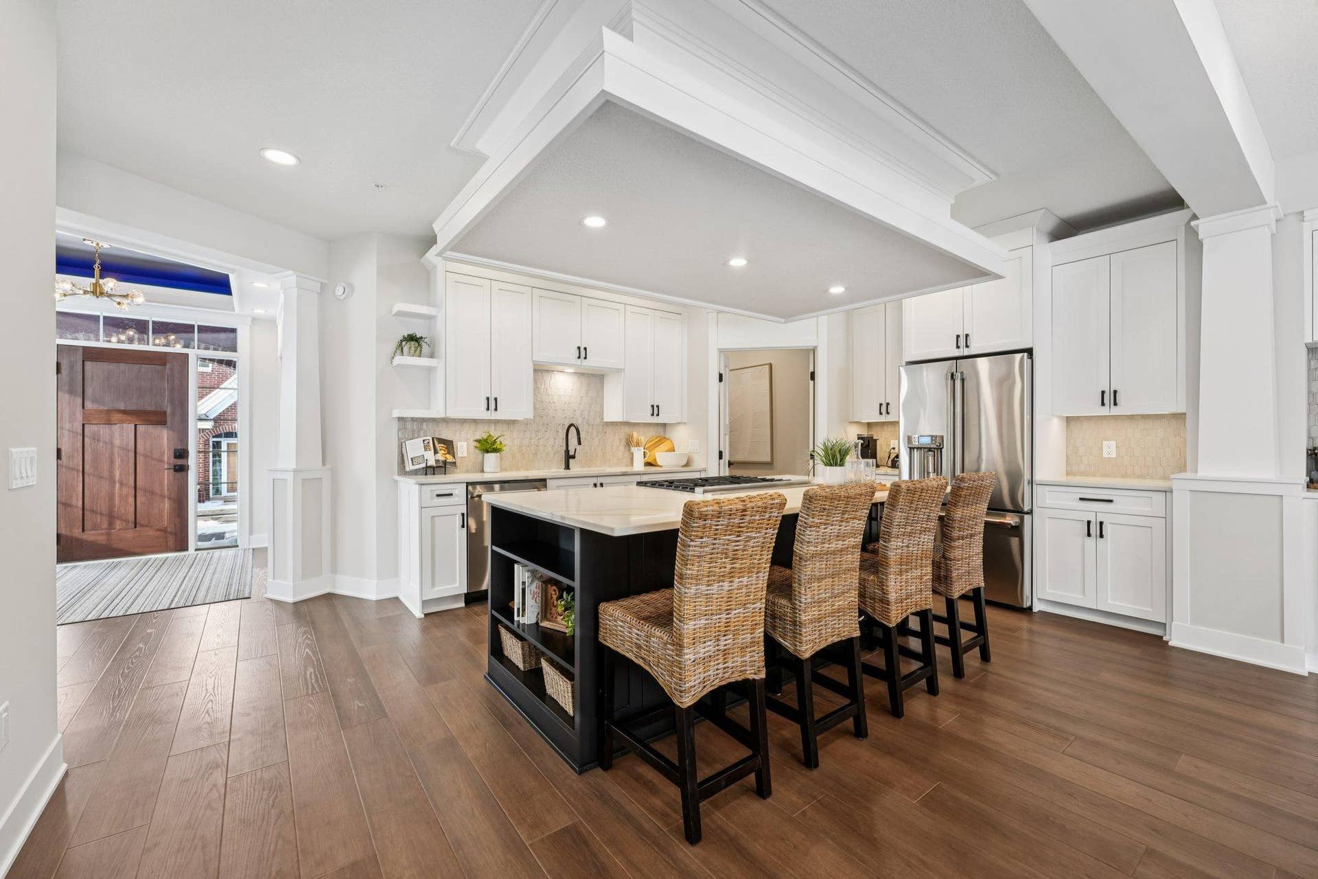 Well-appointed kitchen with white cabinetry, stainless steel appliances, center island with seating, and tile backsplash.