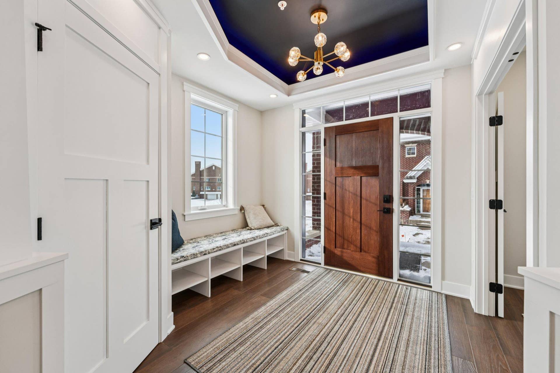 Impressive front entry featuring a tray ceiling with accent paint, designer chandelier, built-in bench seating, and a solid wood front door with sidelights.