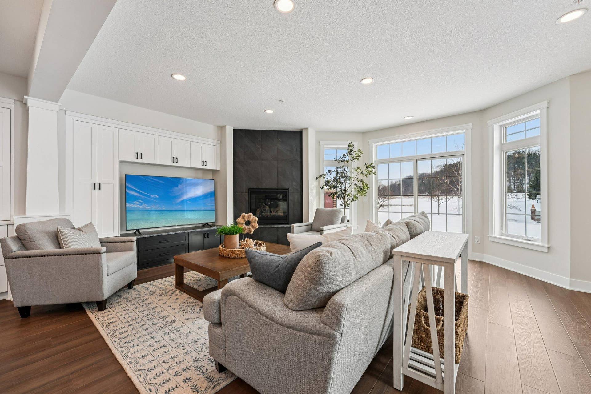 Spacious, light-filled living area featuring hardwood floors, recessed lighting, and a modern corner gas fireplace with tile surround.