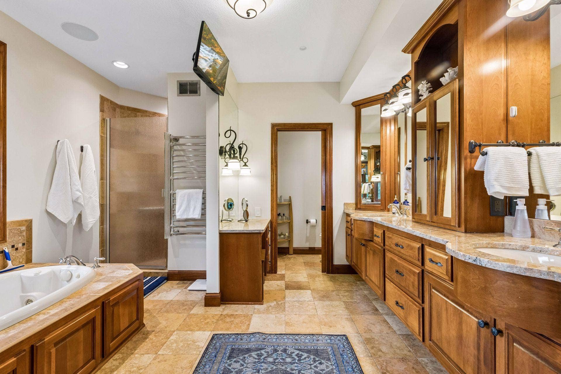 Spa-style primary bath with a soaking tub, walk-in shower, dual vanities, makeup station, private water closet and heated towel warmer
