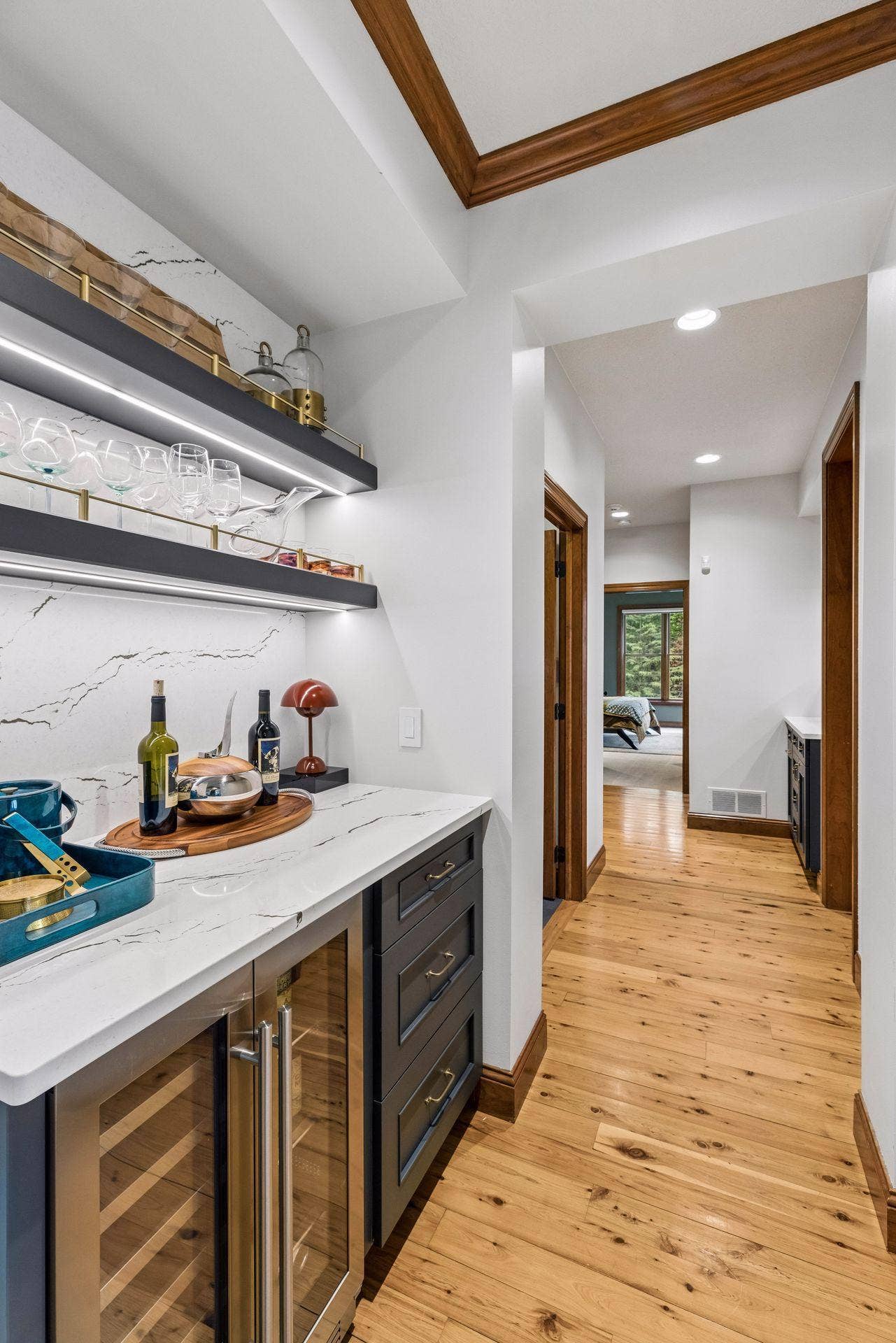 Stylish built-in bar with quartz counters and backsplash, illuminated floating shelves, brass accents, and a beverage fridge, conveniently tucked between the dining area and kitchen