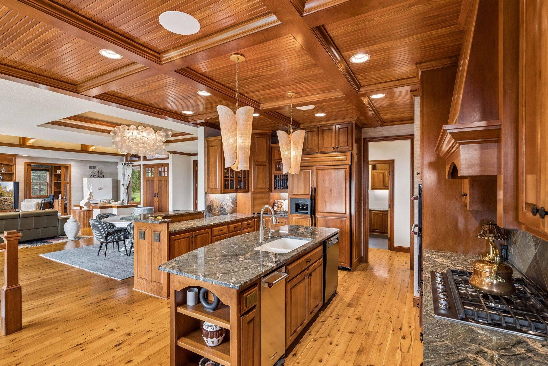Gourmet kitchen with a coffered beadboard ceiling, custom cherry cabinetry, slate backsplash, and granite counters, opening to a cozy keeping room with a stone fireplace and porch access
