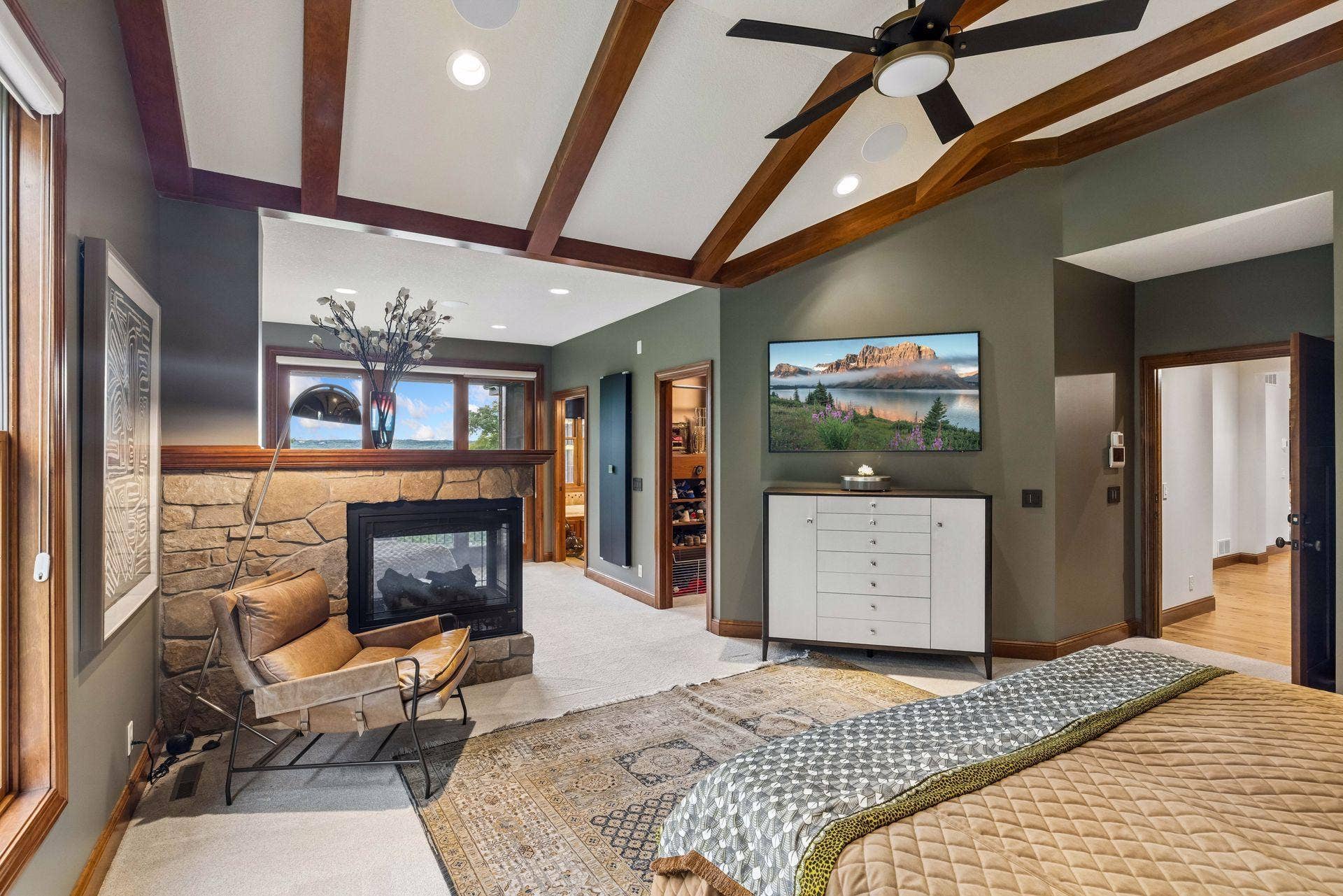 A two-sided stone fireplace connects the bedroom to the sitting area, with a walk-in closet and en suite bath just beyond