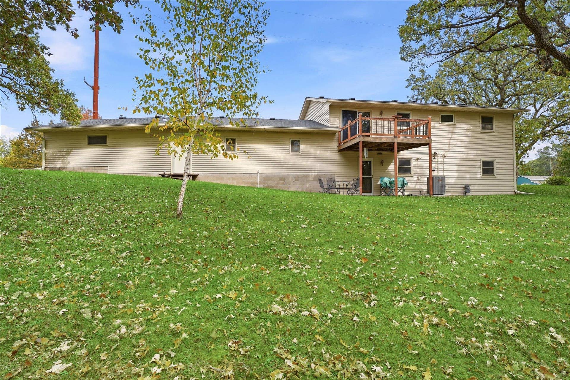 20761 187th Avenue NW, Big Lake, MN 55309 Rear exterior view showcasing the expansive backyard, mature trees, upper-level deck, and lower-level patio with convenient access to the home.