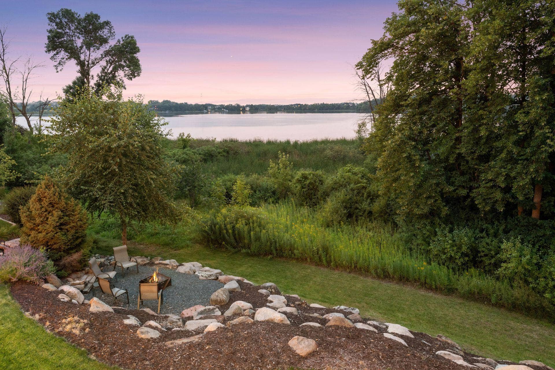 2444 Woods Drive, Victoria, MN 55386 Landscaped backyard features a distinctive boulder feature and firepit area surrounded by a naturalized setting.