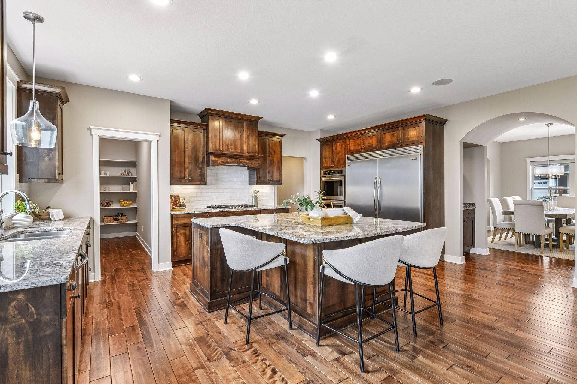 2444 Woods Drive, Victoria, MN 55386 A spacious chef's kitchen pairs rich alder cabinetry with expansive stone countertops, a generous center island with seating, and an easy flow into adjoining informal dining area and great room.