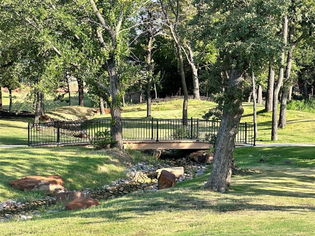 124 Park Avenue, Keller, TX 76262 Landscaped green space featuring a pedestrian bridge with black railings, a stone-lined creek bed, and mature trees