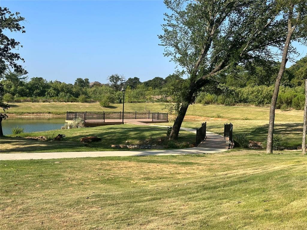 300 Park Avenue, Keller, TX 76262 Waterfront decking with black metal railing, concrete pathway, and wooden bridge, all surrounded by green landscaping