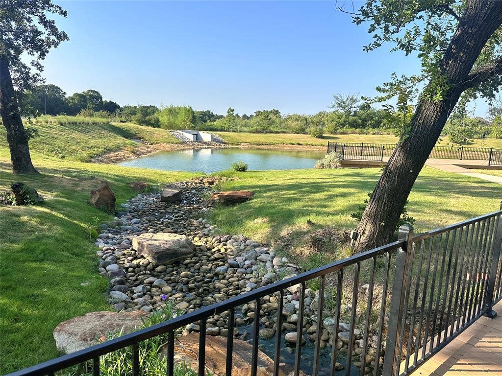 300 Park Avenue, Keller, TX 76262 Landscaped green space featuring a pedestrian bridge with black railings, a stone-lined creek bed, and mature trees